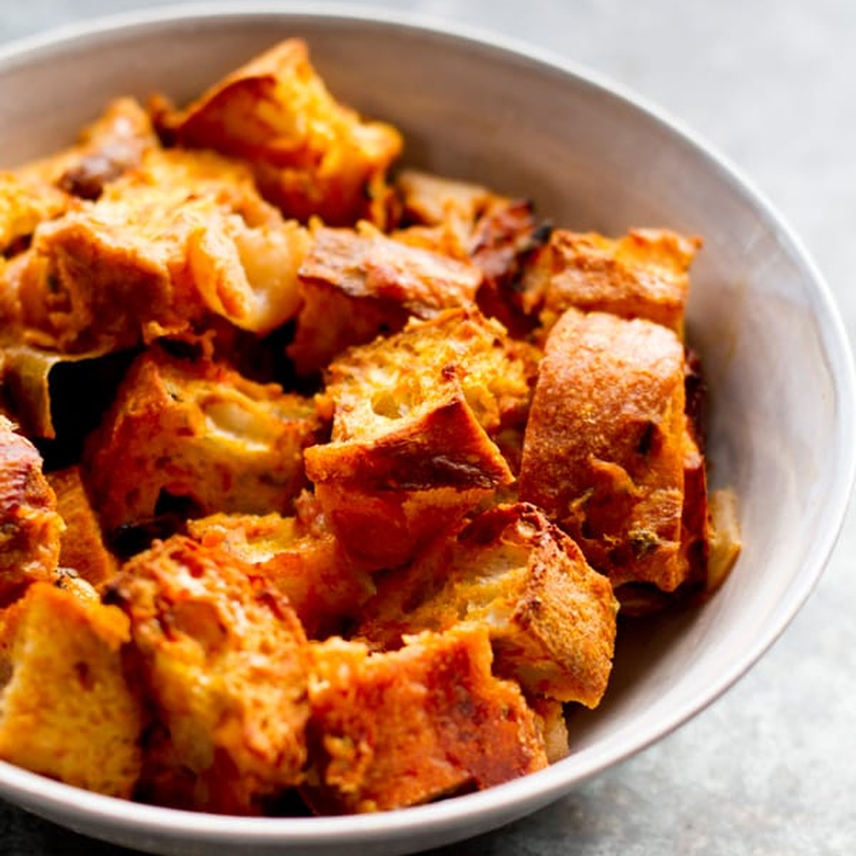 Cheddar pumpkin stuffing with golden bread cubes in a white bowl