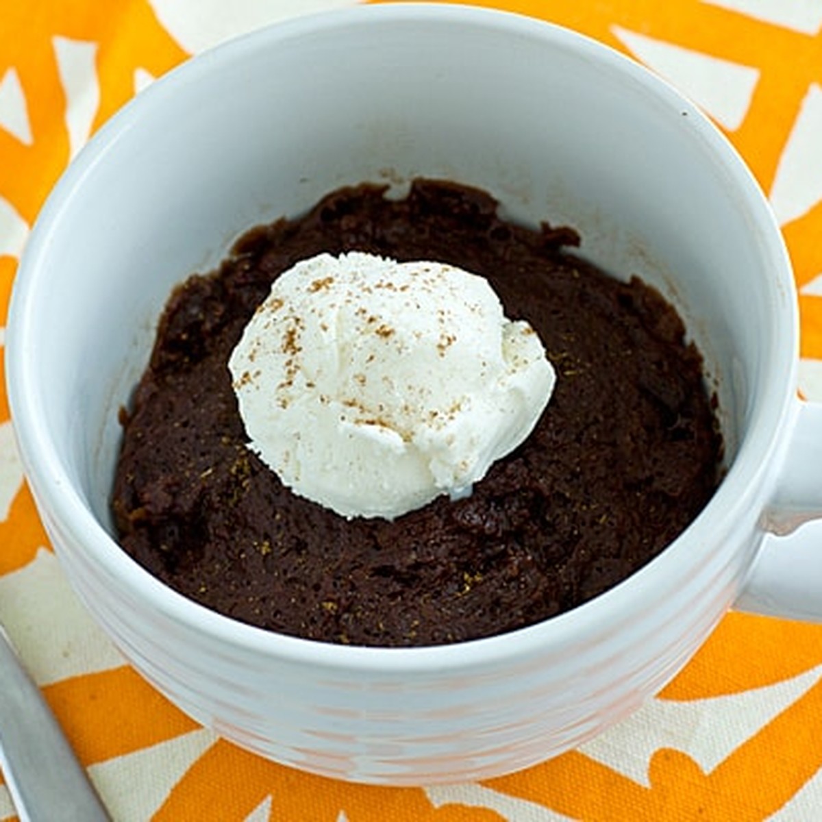 Chocolate pumpkin mug cake in a white mug topped with a scoop of vanilla ice cream and pumpkin pie spice