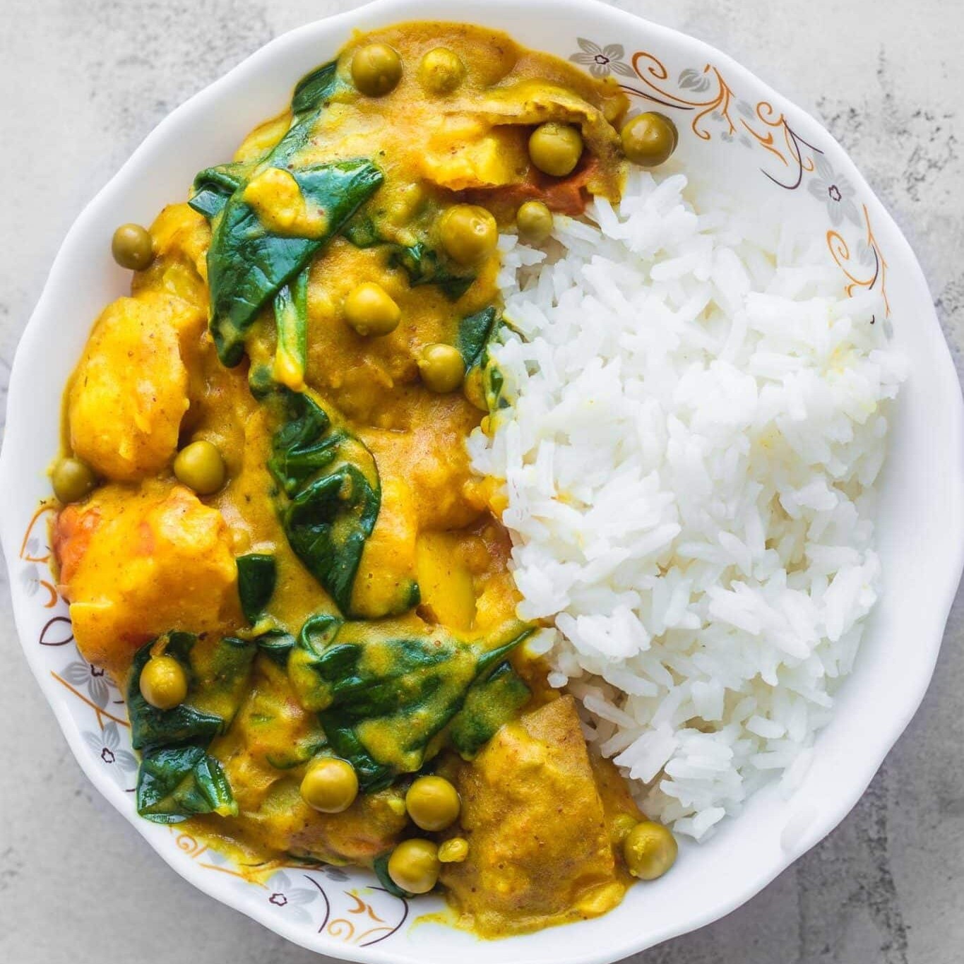 Easy vegan potato curry with spinach, peas and rice in a white bowl