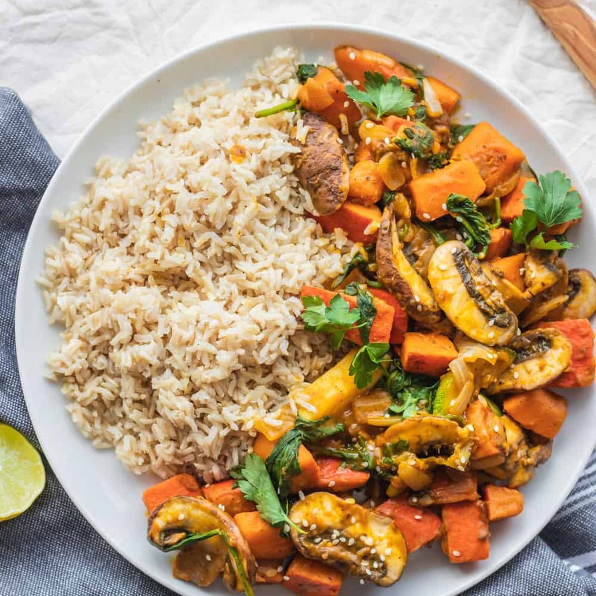 Pumpkin stir-fry with mushrooms, zucchini and spinach next to brown rice on a white plate