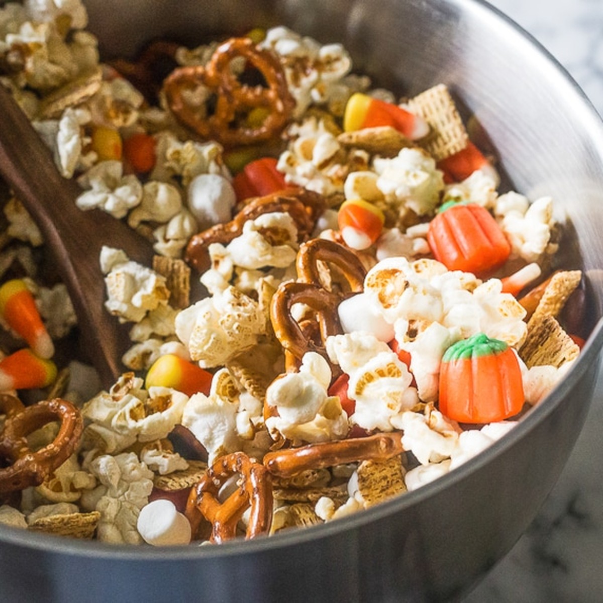 Fall snack mix with popcorn, pretzels, Chex, candy corn and candy pumpkins in a mixing bowl