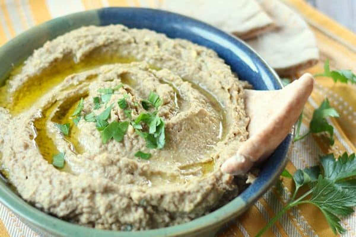 Bowl of green lentil hummus with olive oil, chopped parsley and a pita wedge for dipping