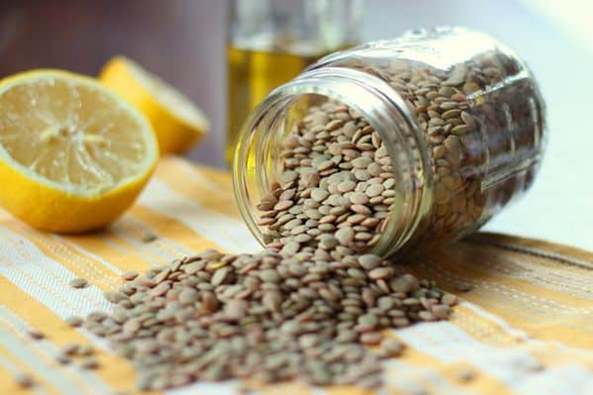 Dried green lentils spilling from a glass jar next to a halved lemon