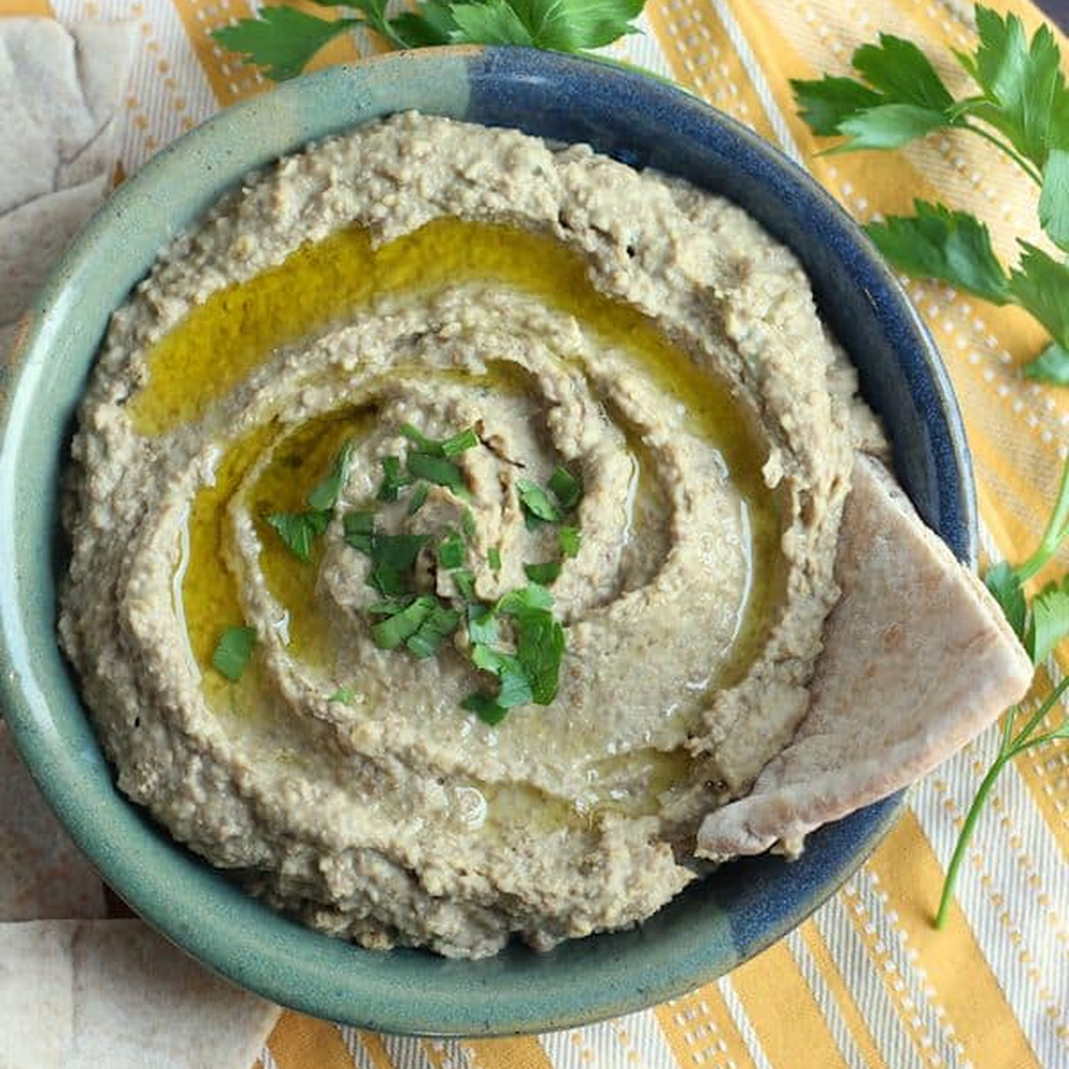 Green lentil hummus in a blue-green bowl drizzled with olive oil and parsley, served with pita
