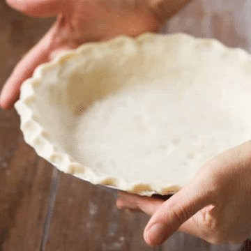 Homemade coconut oil pie crust pressed into a pie plate and held in two hands