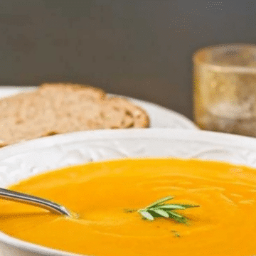 Honey roasted butternut pumpkin soup in a white bowl with a spoon and crusty bread