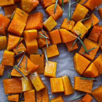 Roasted butternut squash cubes with fresh rosemary on a parchment-lined baking tray