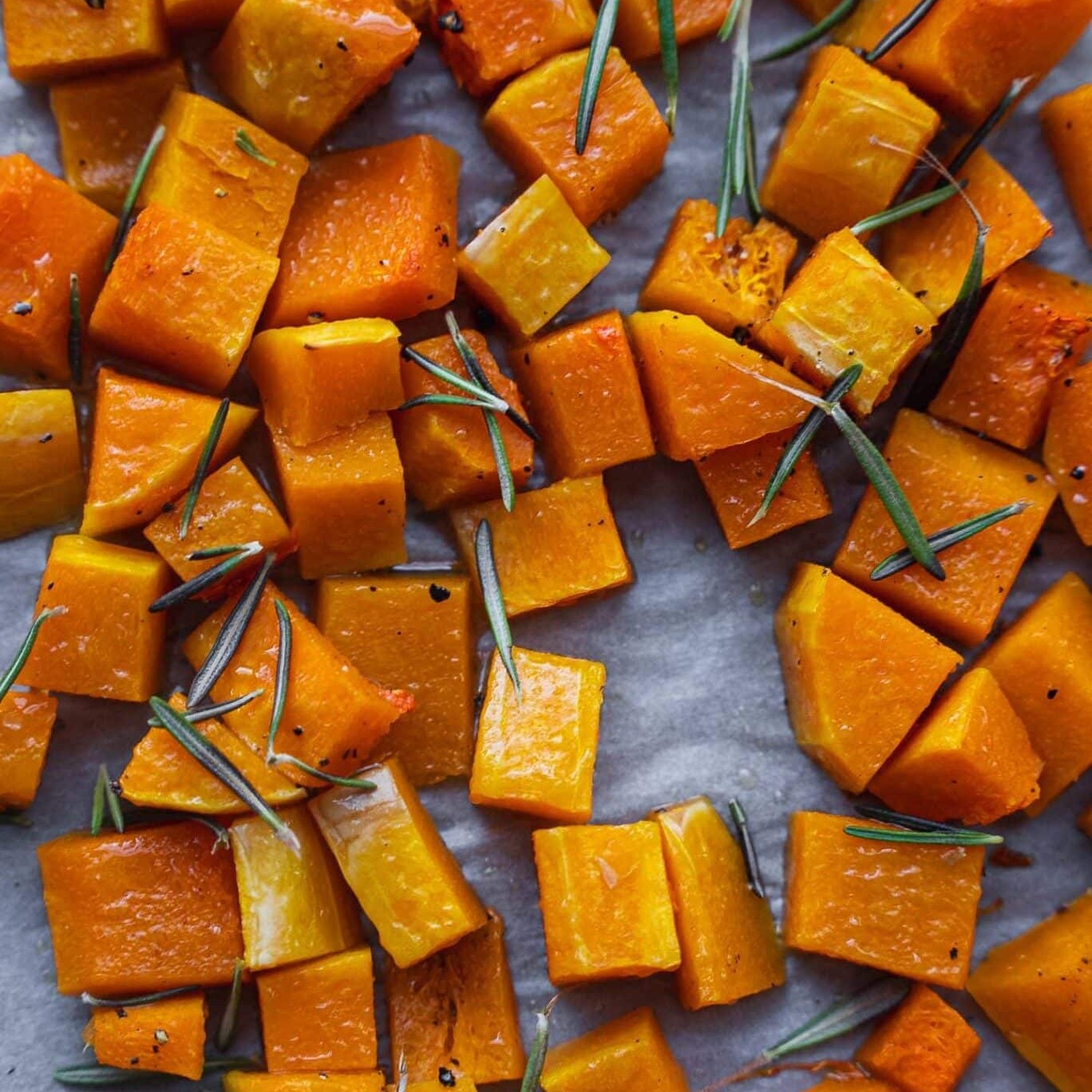 Roasted butternut squash cubes with fresh rosemary on a baking tray