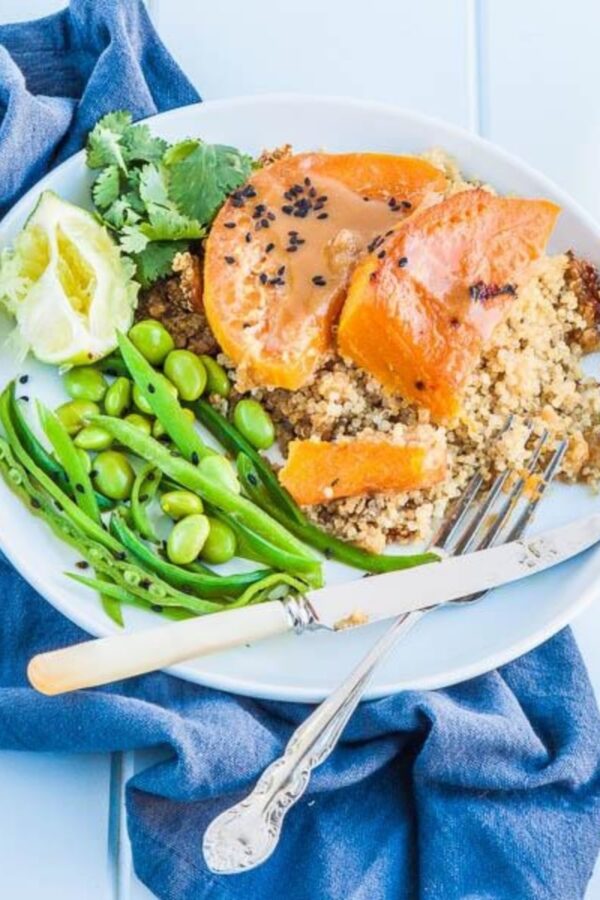 Miso glazed pumpkin slices on quinoa with edamame, snow peas, cilantro and lime on a white plate