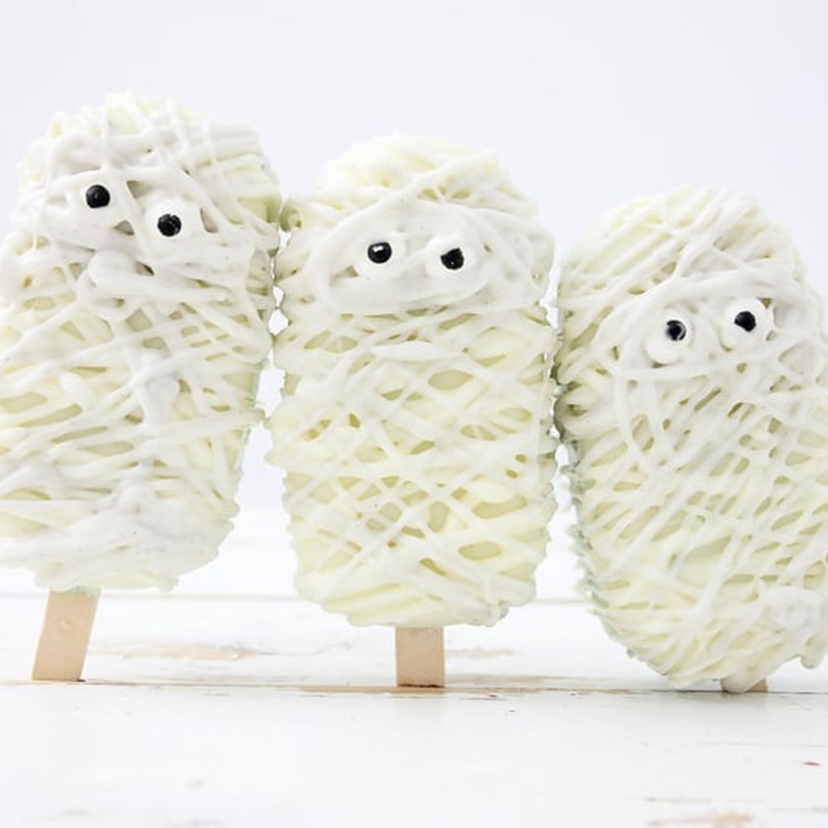Three mummy cakesicles standing on popsicle sticks against a white background
