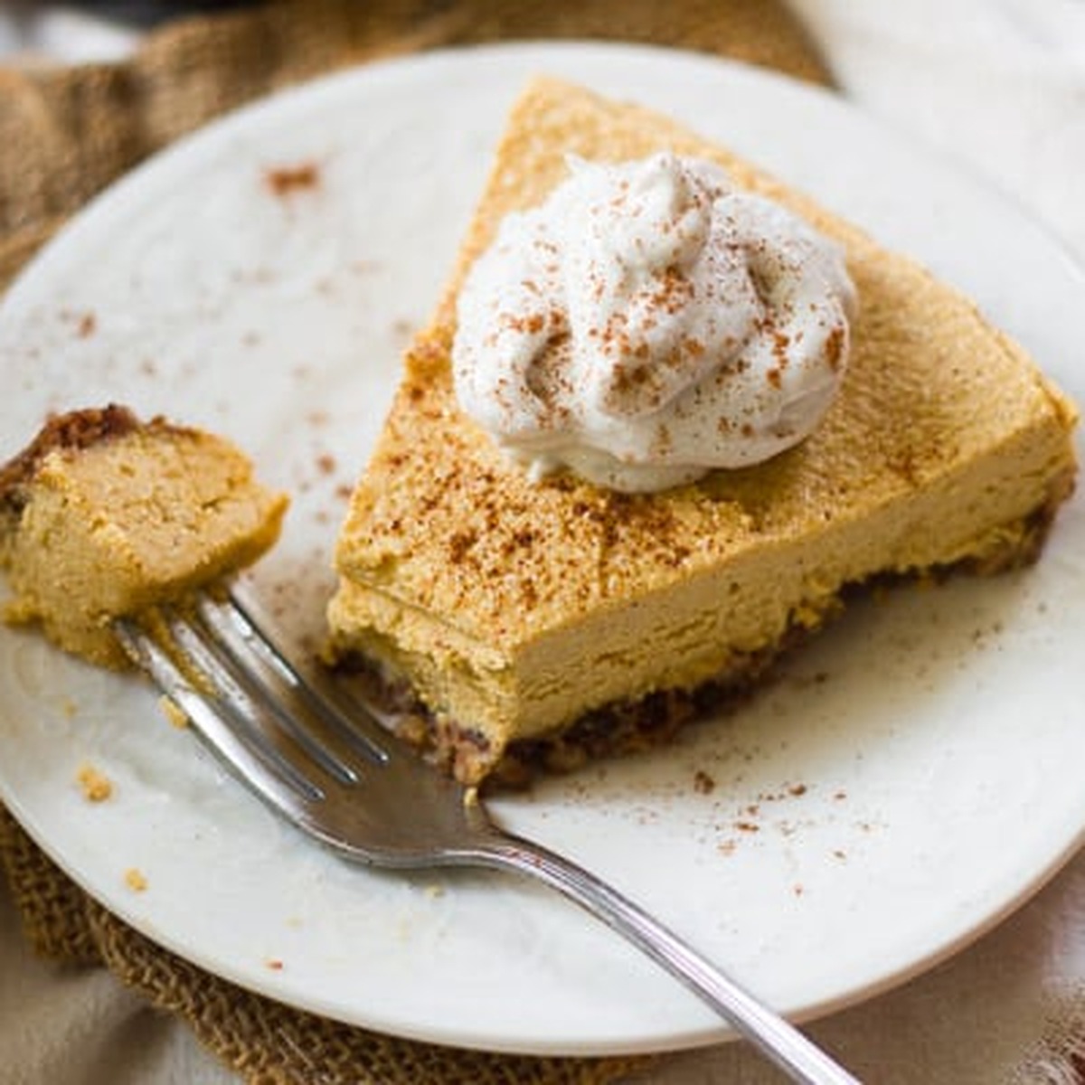 Slice of no-bake vegan pumpkin cheesecake with coconut whipped cream and cinnamon on a white plate