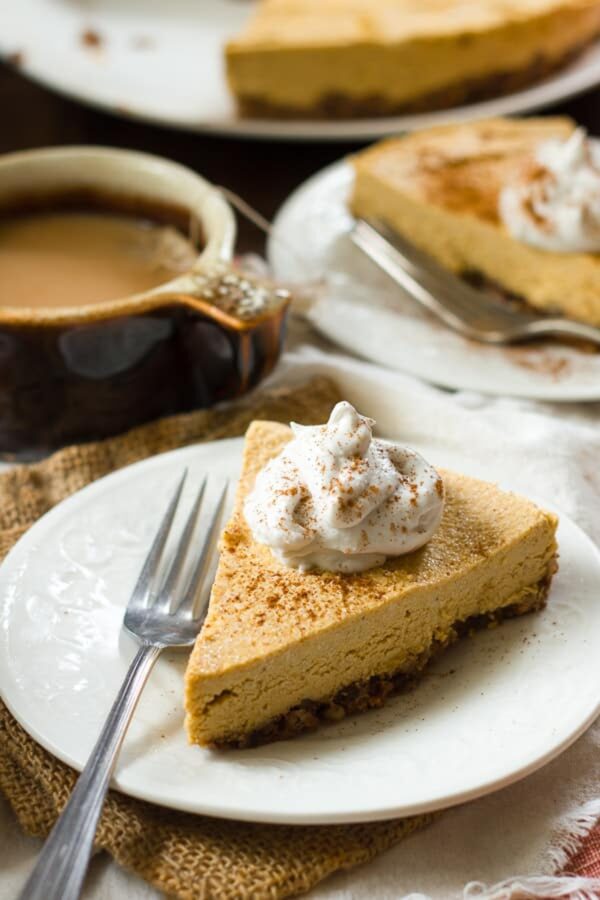 Slice of vegan pumpkin cheesecake with a pecan-date crust and coconut whipped cream