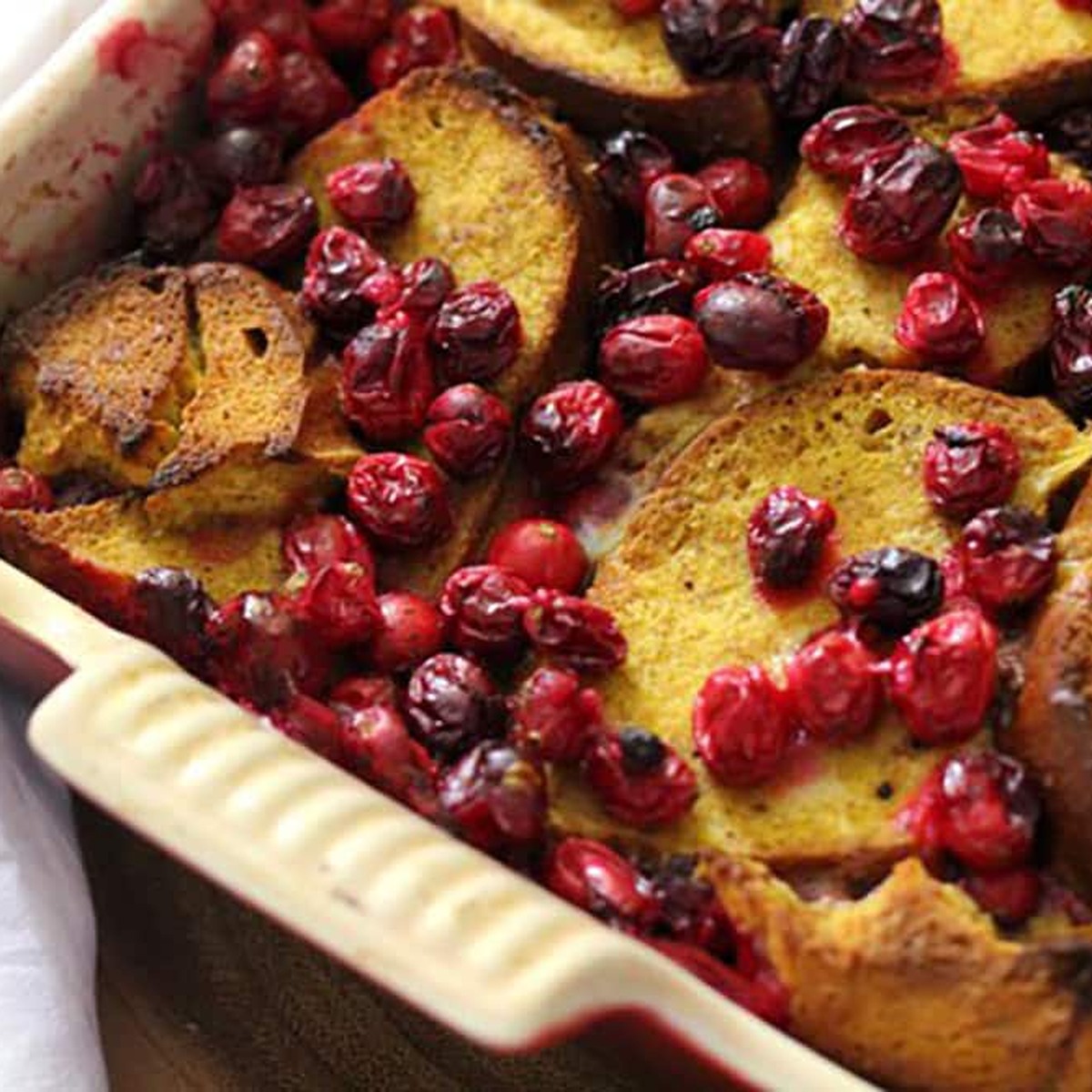 Overnight pumpkin French toast casserole with roasted cranberries, square close-up