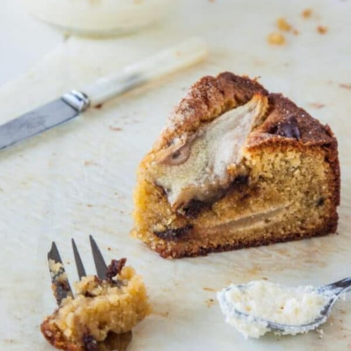 Slice of pear, chocolate and cardamom cake on parchment with a fork and a spoonful of cream