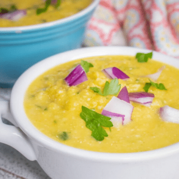 Pumpkin cauliflower rice soup in a white bowl topped with parsley and red onion