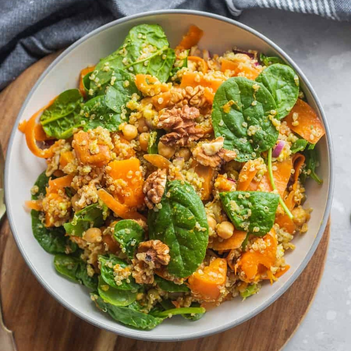 Pumpkin chickpea quinoa bowl with roasted pumpkin, baby spinach, carrot ribbons and walnuts in a white bowl