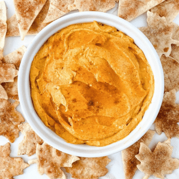 Pumpkin cream cheese dip in a white bowl surrounded by cinnamon sugar chips