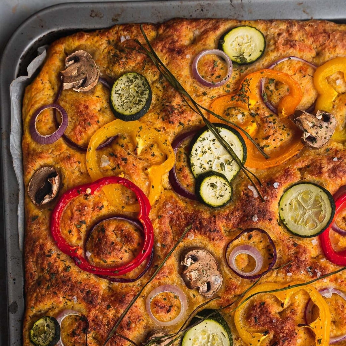 Square slab of pumpkin focaccia bread topped with peppers, zucchini, mushrooms and red onion