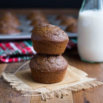 Pumpkin gingerbread muffins stacked on parchment with a bottle of milk