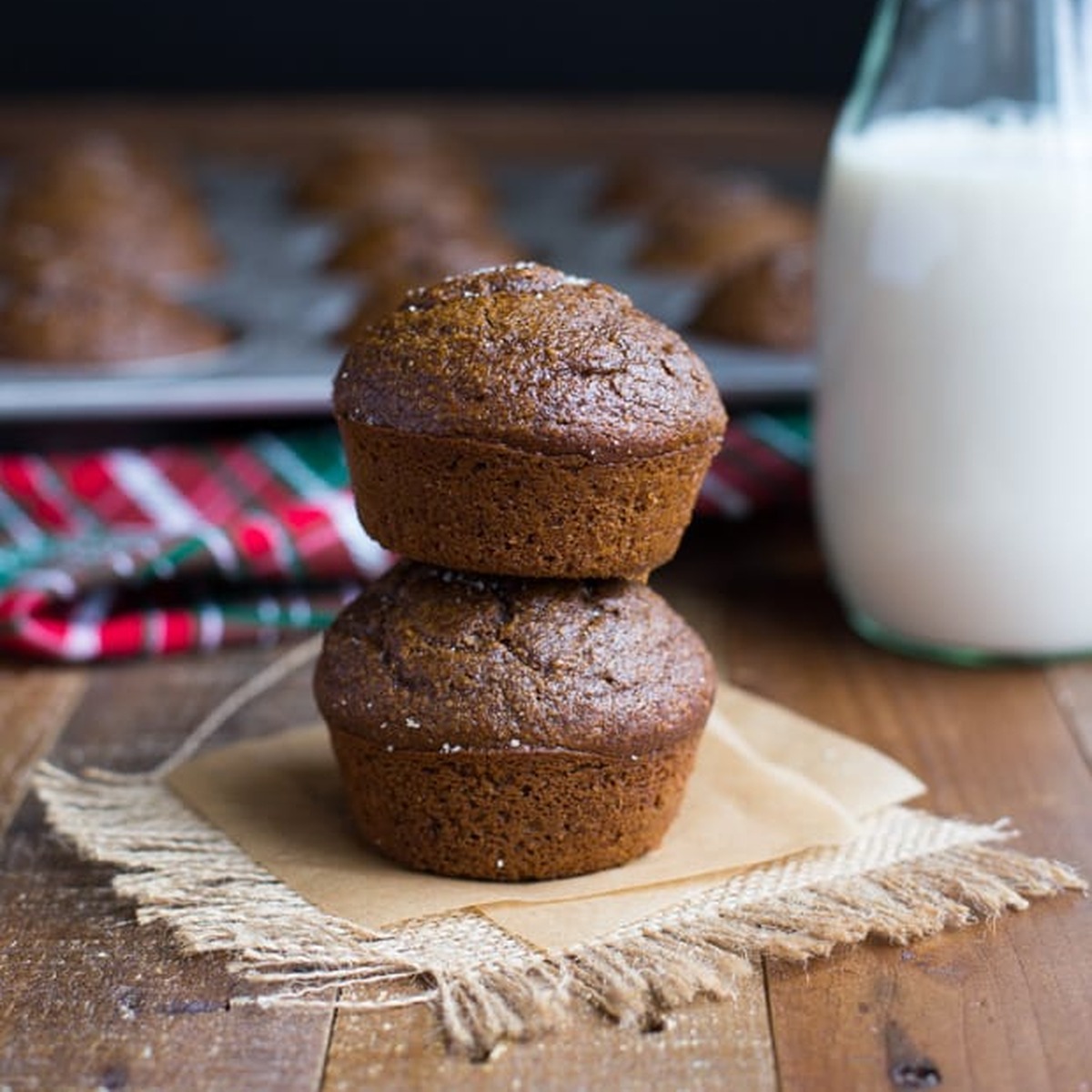 Two pumpkin gingerbread muffins stacked on parchment and burlap with a bottle of milk behind