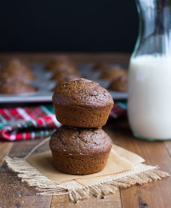 Stacked pumpkin gingerbread muffins with a pan of muffins and a bottle of milk in the background
