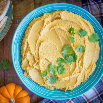 Bowl of 10-minute pumpkin hummus topped with cilantro, with pita bread and a mini pumpkin
