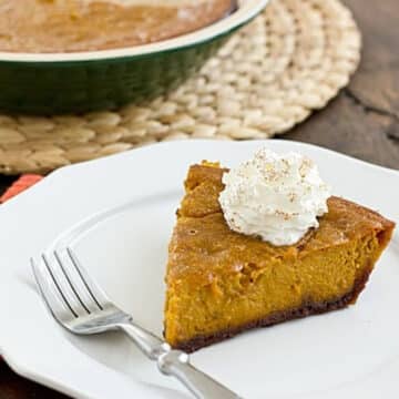 Slice of pumpkin pie with gingersnap crust topped with whipped cream on a white plate