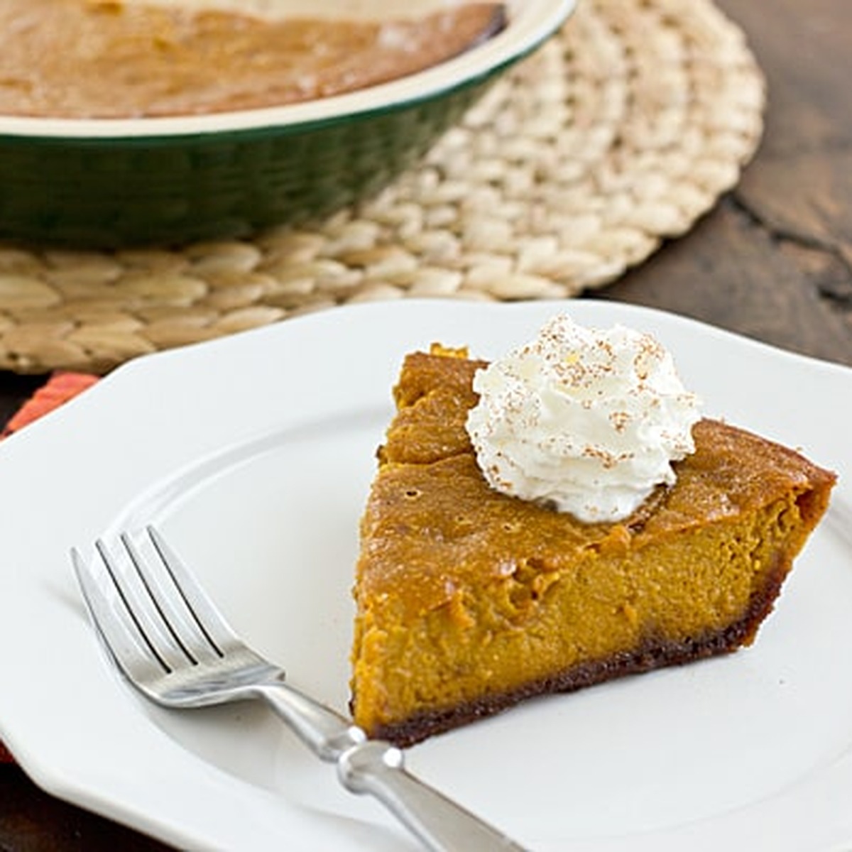 Slice of pumpkin pie with gingersnap crust topped with whipped cream and cinnamon on a white plate with a fork