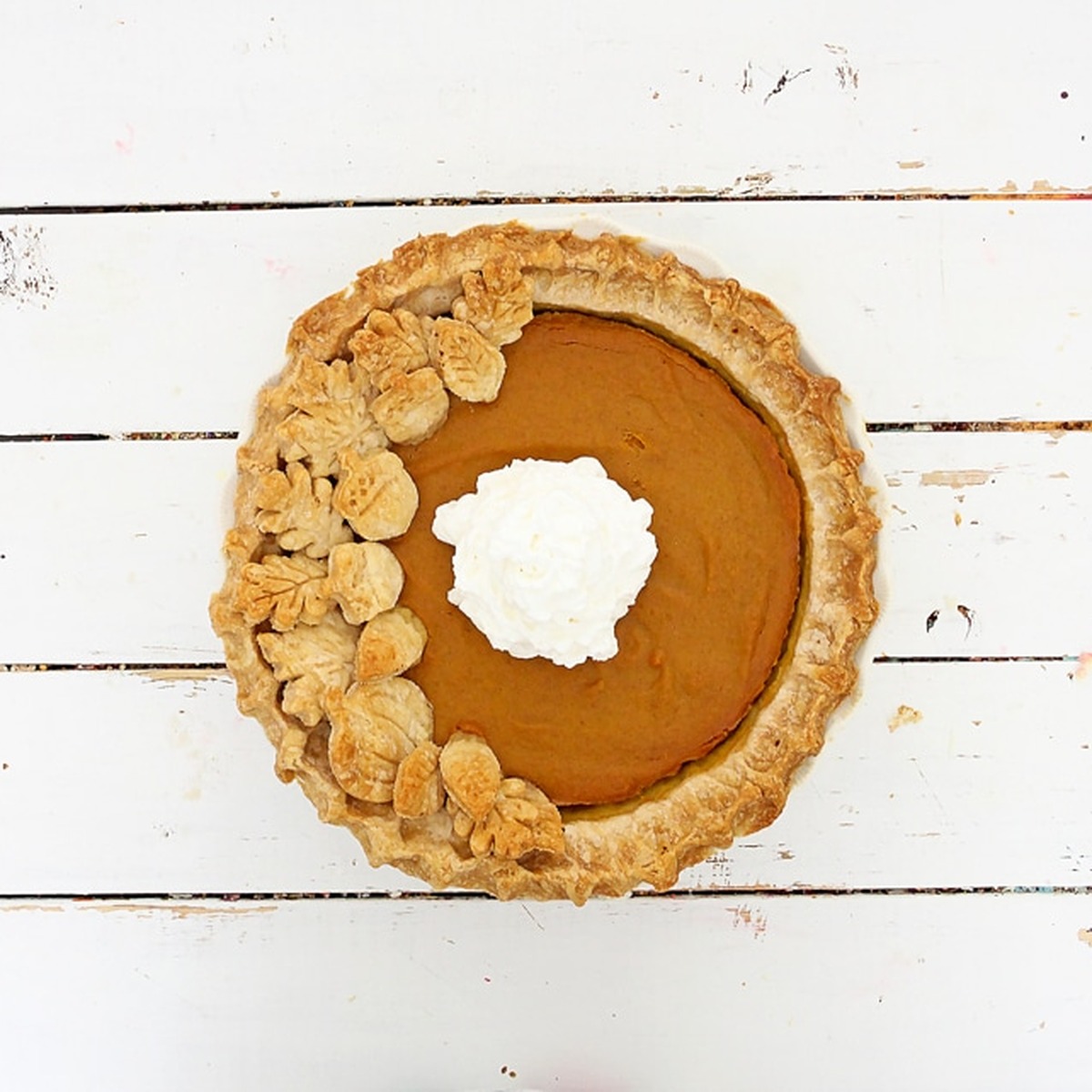 Overhead view of a pumpkin pie with a homemade crust decorated with pastry leaves and topped with whipped cream