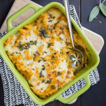 Pumpkin sage baked ziti in a green baking dish topped with melted cheese and crispy sage