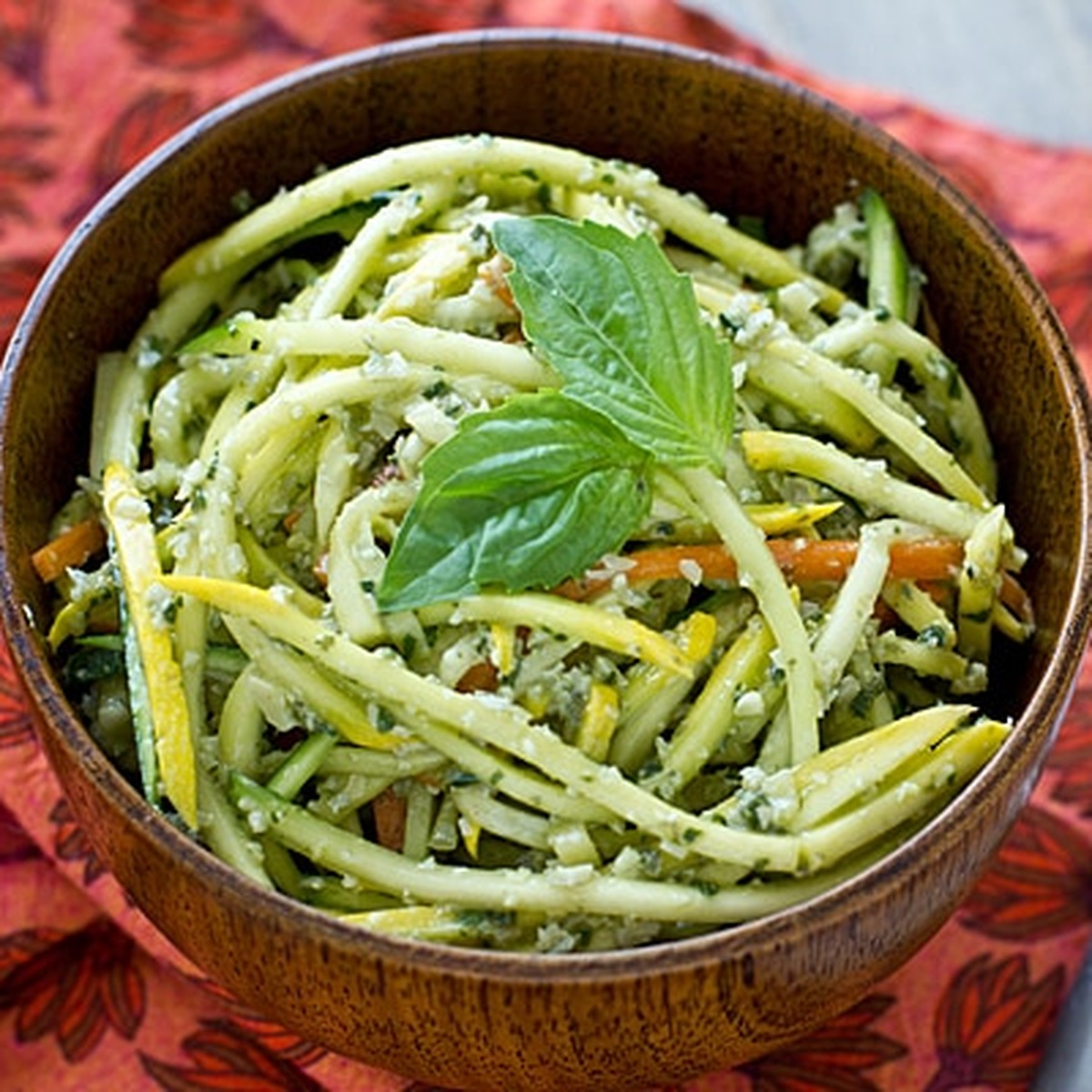 Pumpkin seed pesto tossed with yellow squash, zucchini and carrot noodles in a wooden bowl, topped with fresh basil