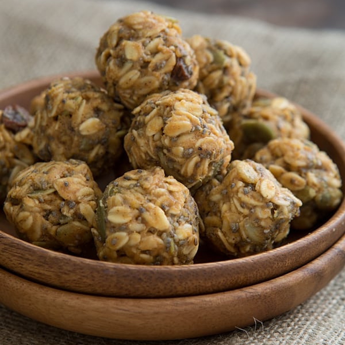 Pumpkin spice energy bites stacked in a wooden bowl on burlap