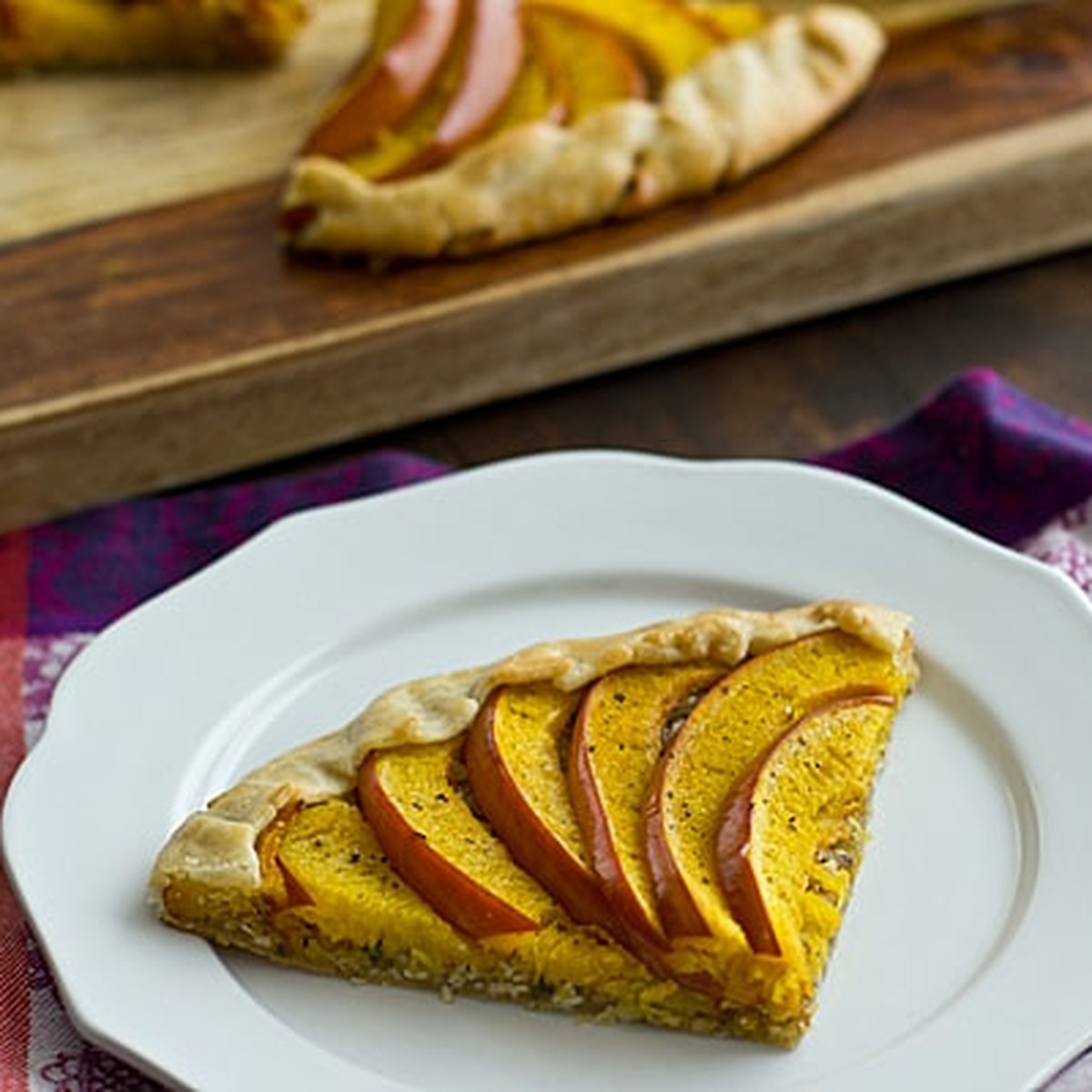 Slice of savory pumpkin galette with roasted pumpkin wedges on a white plate