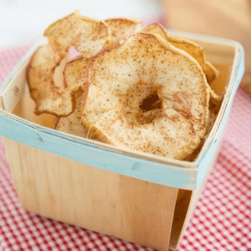 Soft and chewy spiced dried apple rings piled in a wooden berry basket on a red gingham cloth