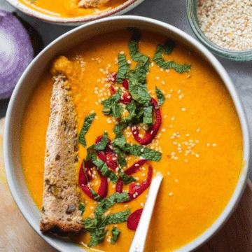 Bowl of spicy butternut squash soup topped with red chili, mint and sesame seeds