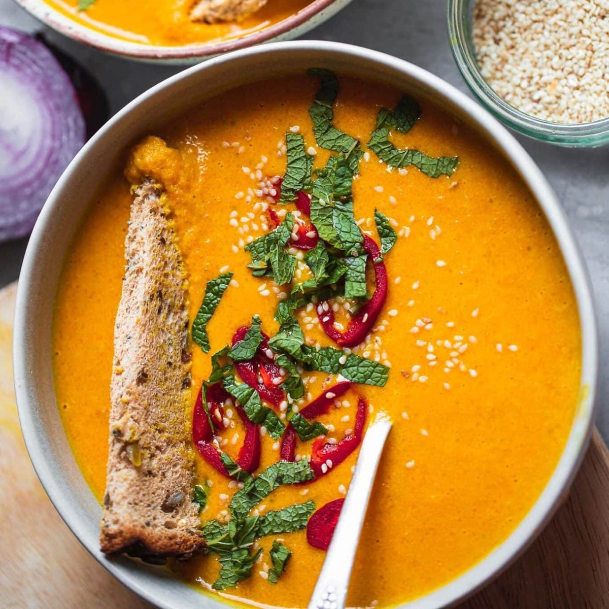 Bowl of spicy butternut squash soup topped with red chili, fresh mint, sesame seeds and a slice of crusty bread