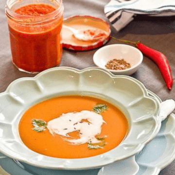 Spicy white bean pumpkin soup in a pale blue bowl with coconut milk and cilantro, with a jar of homemade harissa
