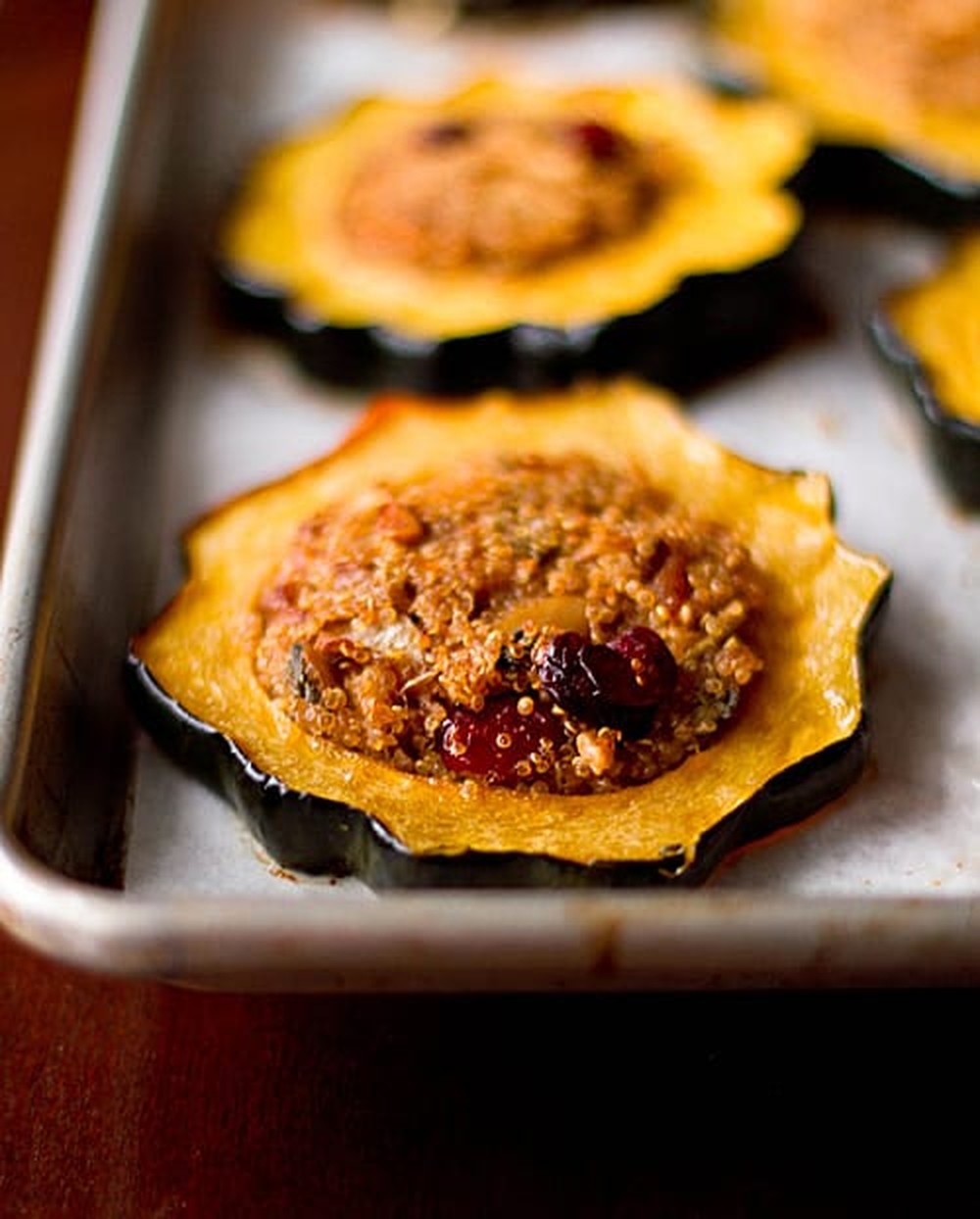 Close-up of a baked acorn squash ring filled with quinoa, cranberries and walnuts on a baking sheet