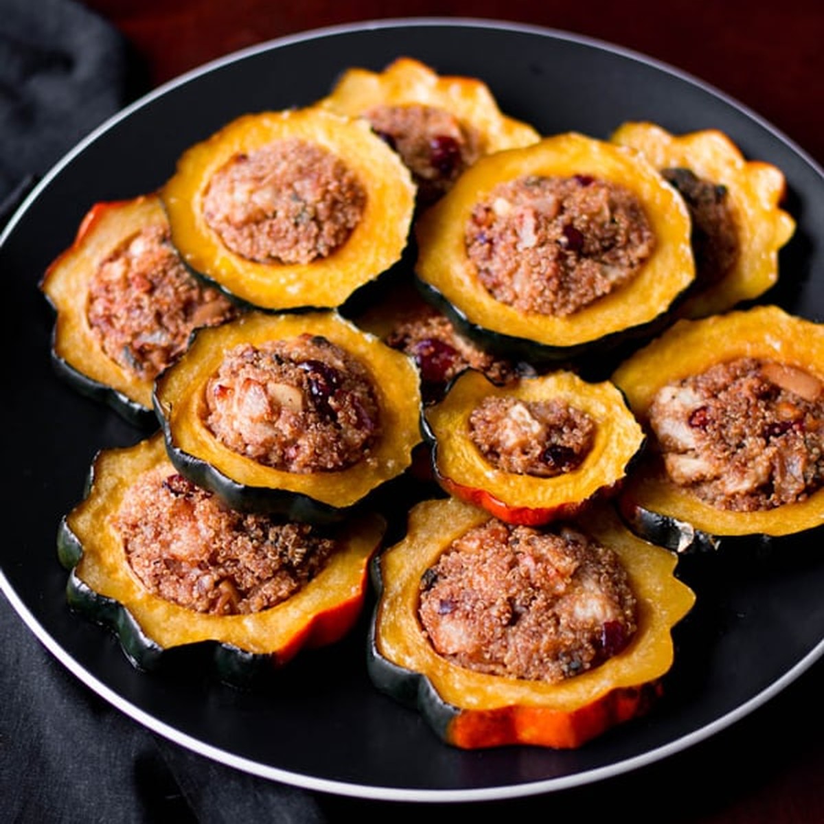 Quinoa-stuffed acorn squash rings arranged on a round black plate