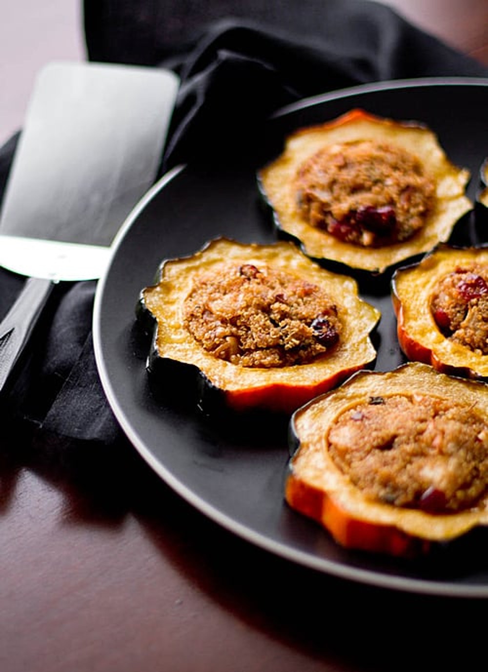 Stuffed acorn squash rings on a black plate next to a metal spatula