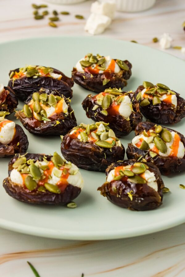 Whipped feta stuffed Medjool dates topped with hot honey, pumpkin seeds and lemon zest on a green plate