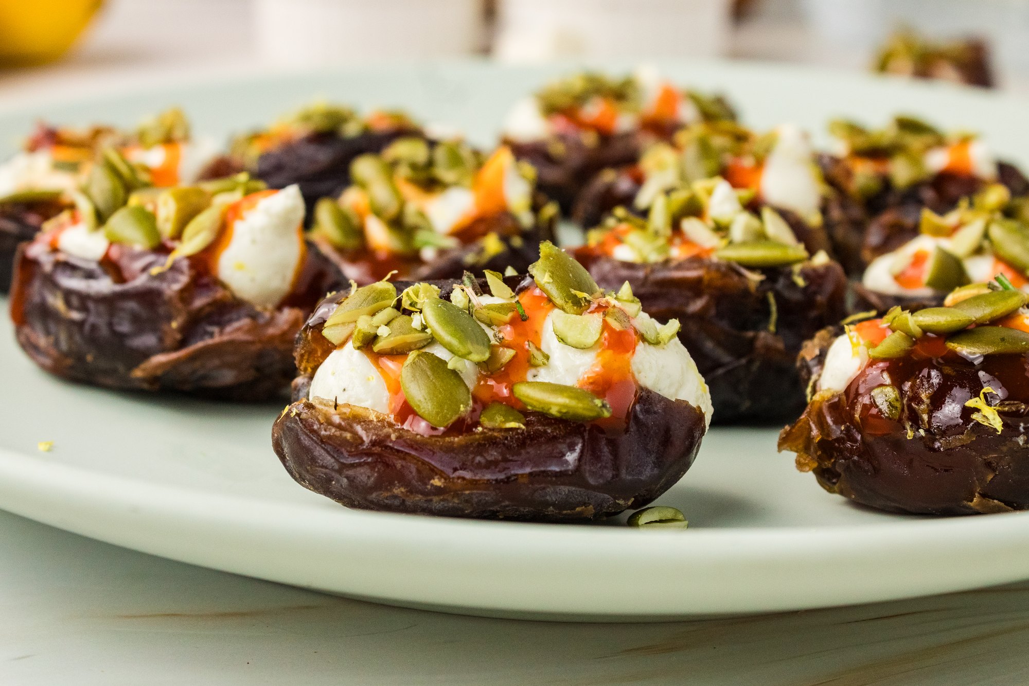 Side view of whipped feta stuffed dates with hot honey and pumpkin seeds on a green serving plate