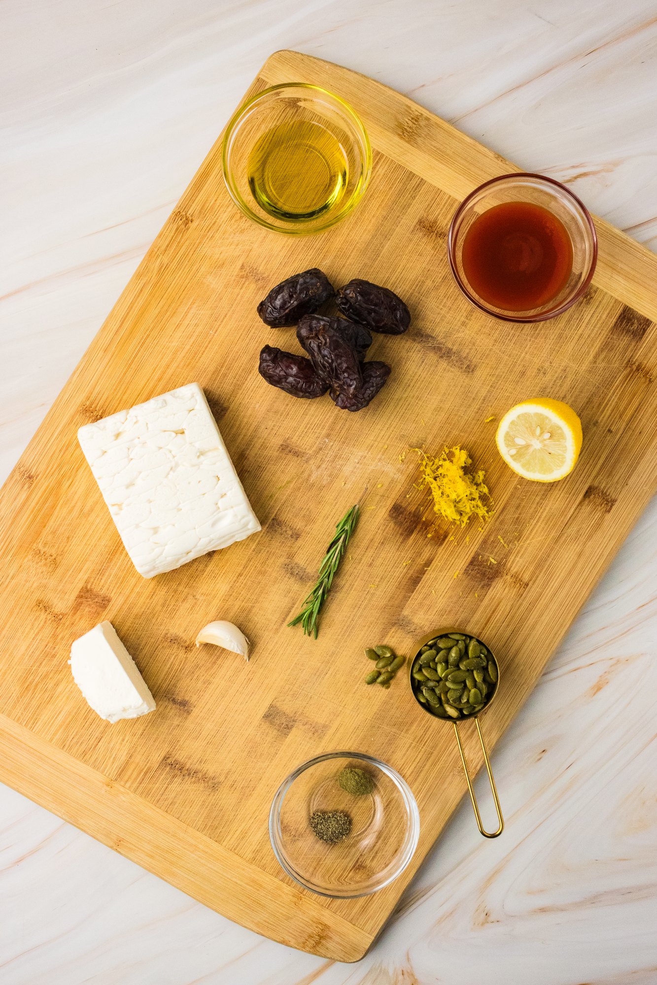 Ingredients for whipped feta stuffed dates on a cutting board: feta, cream cheese, Medjool dates, hot honey, lemon, garlic, rosemary and pumpkin seeds