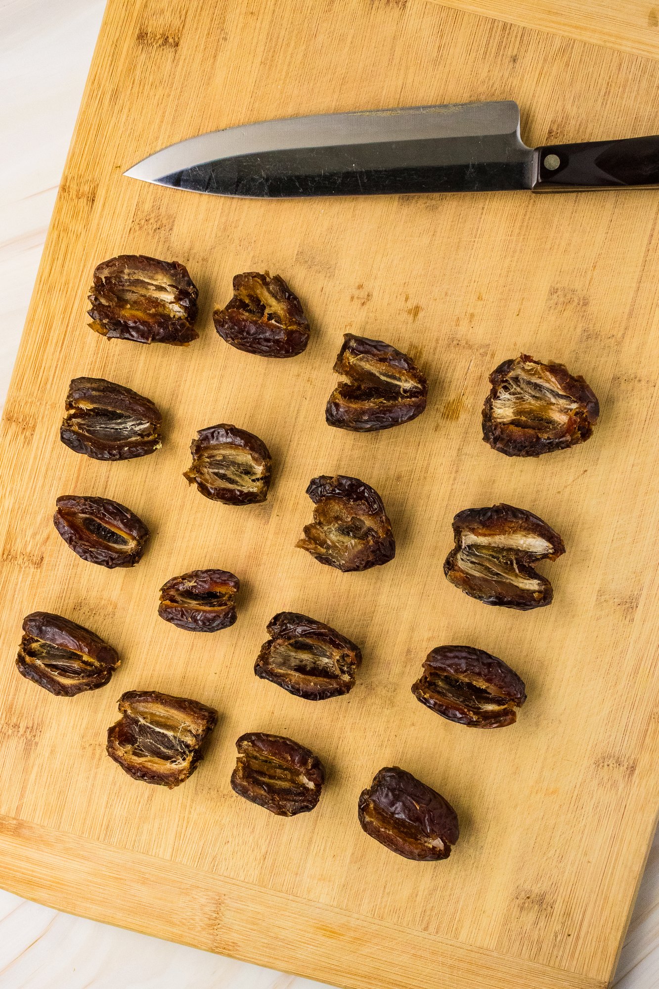 Medjool dates sliced open and pitted on a wooden cutting board with a chef knife