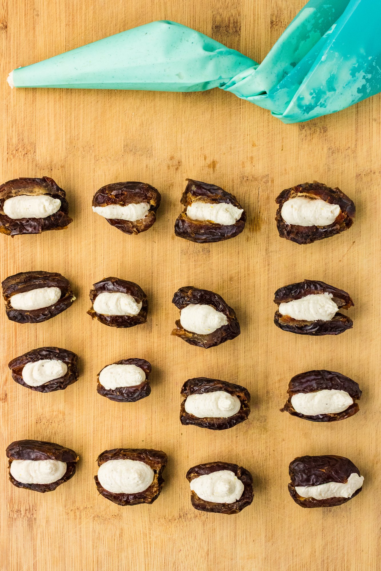 Pitted Medjool dates filled with piped whipped feta on a cutting board next to a piping bag