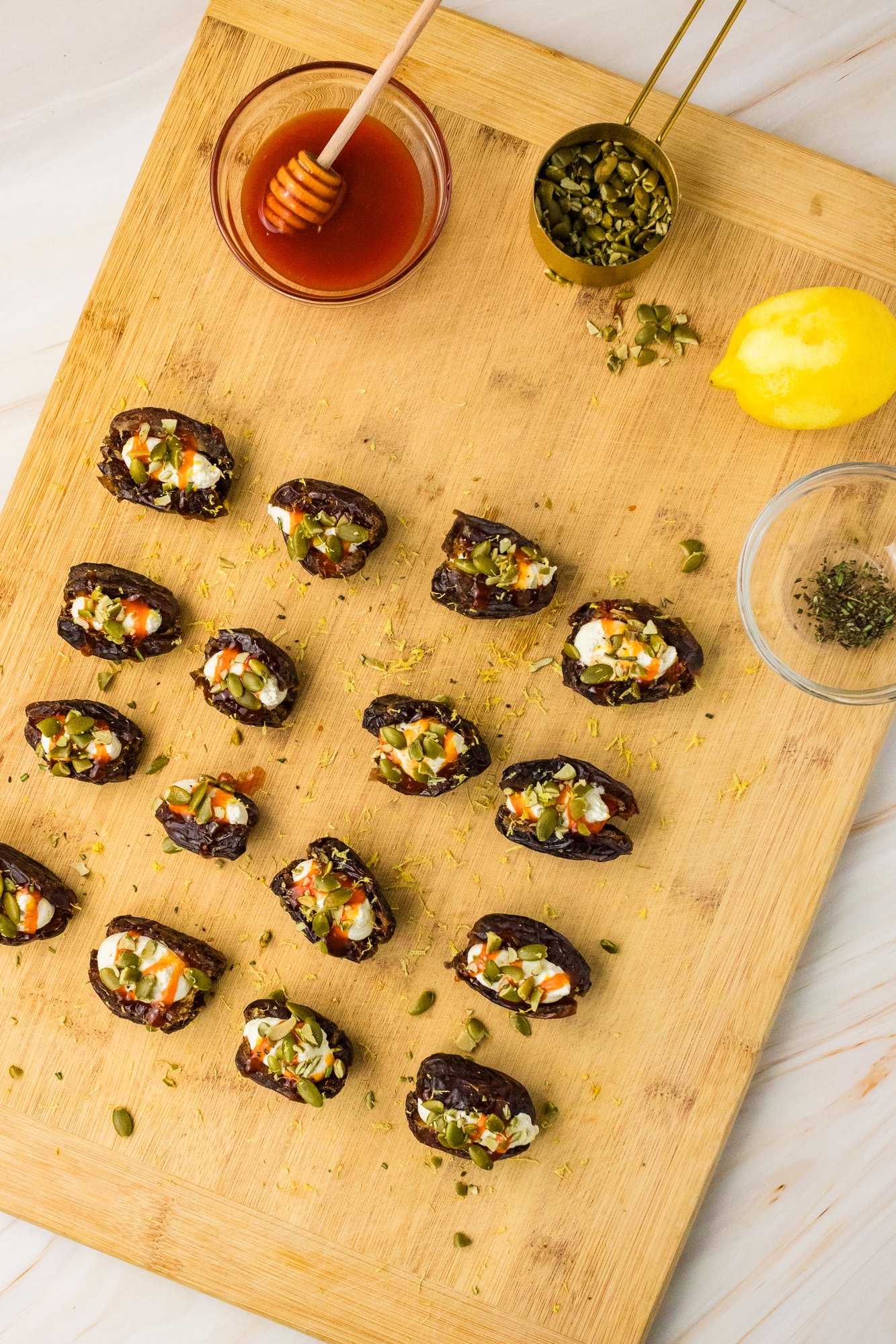 Whipped feta stuffed dates topped with pumpkin seeds on a cutting board with hot honey and lemon