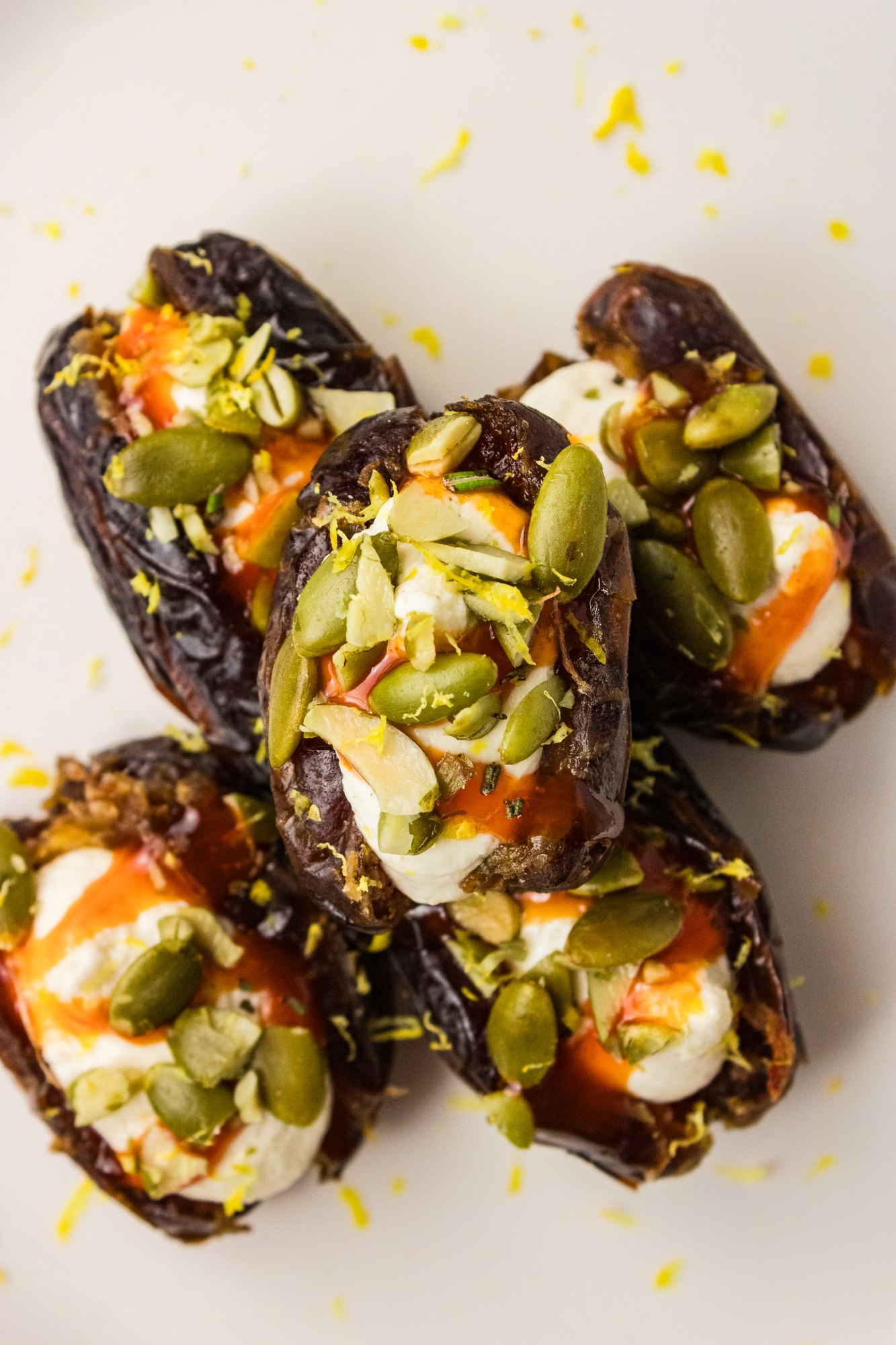 Overhead close-up of stacked stuffed dates with whipped feta, hot honey drizzle, pumpkin seeds and lemon zest