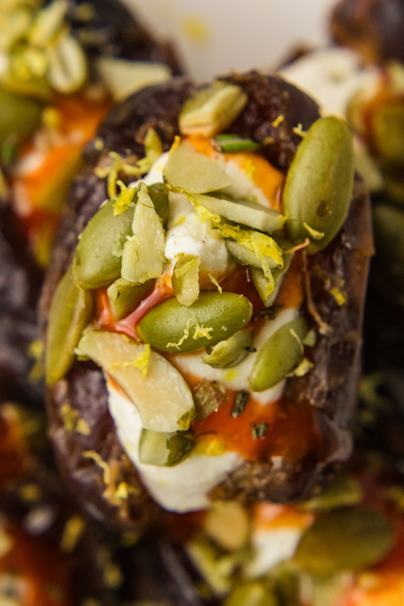 Macro close-up of a Medjool date stuffed with whipped feta, hot honey and chopped pumpkin seeds