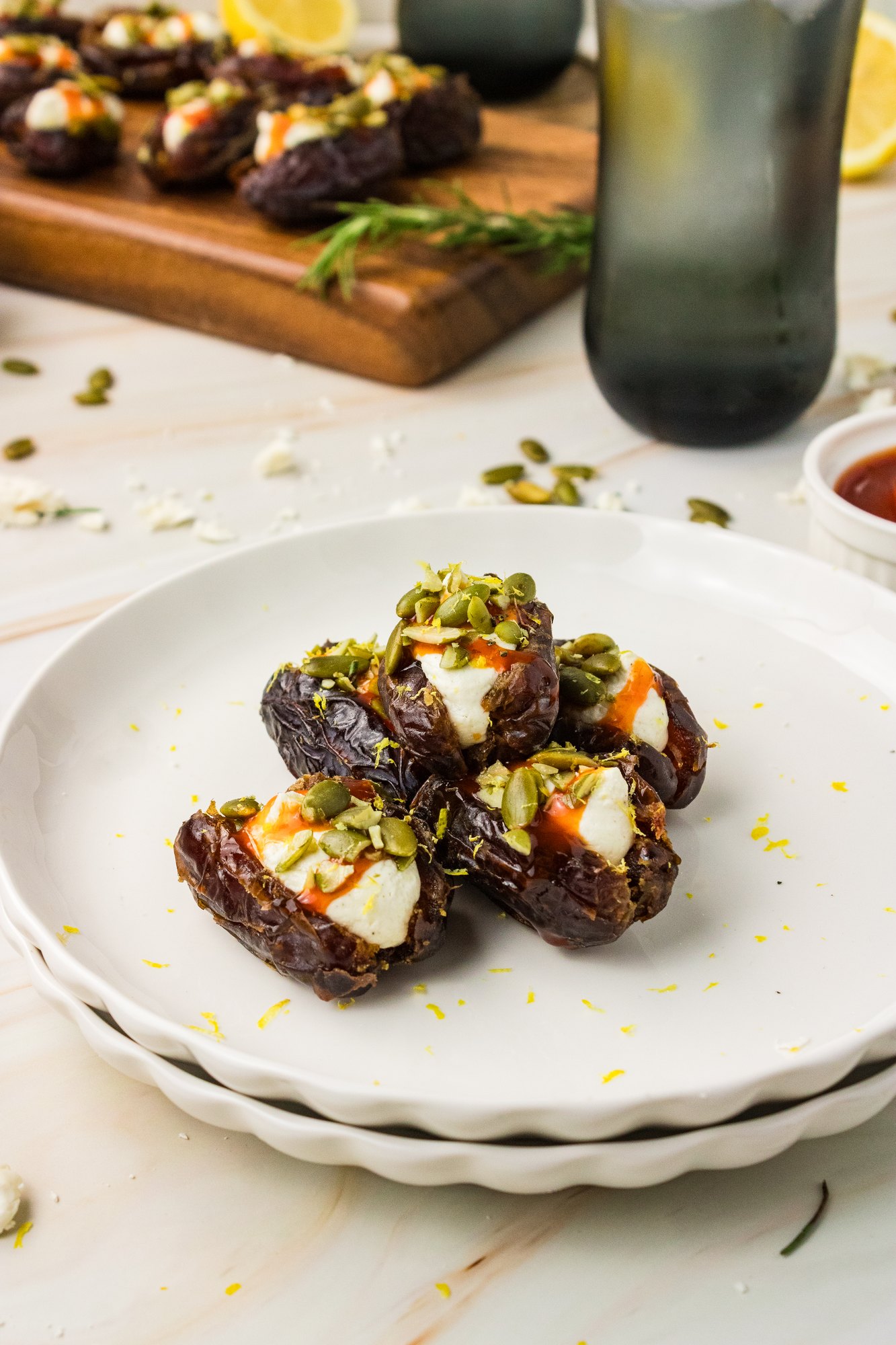 Whipped feta stuffed dates stacked on small white plates with drinks and more dates in the background