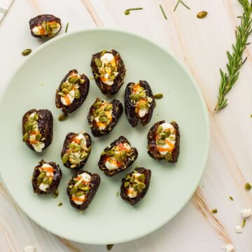 Overhead view of whipped feta stuffed dates with hot honey and pumpkin seeds on a pale green plate